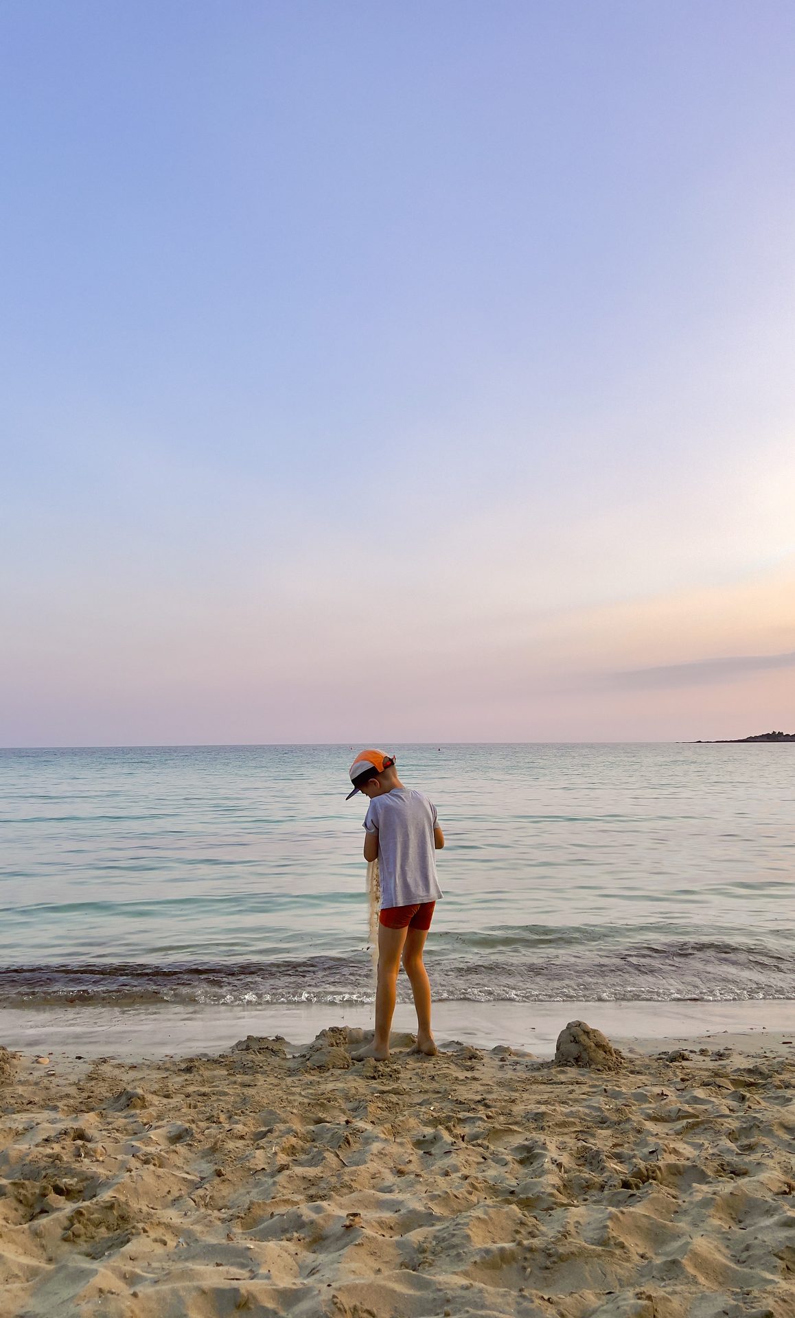 A child building sandcastles at the shoreline at dusk