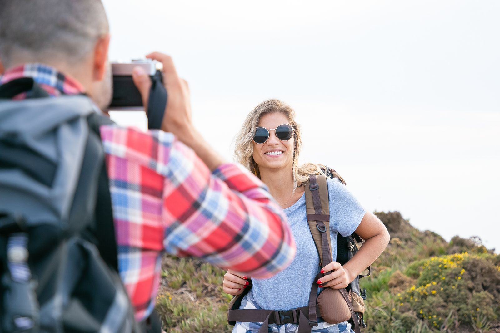 A smiling hiker with a backpack as her travel companion photographs her on a coastal trail
